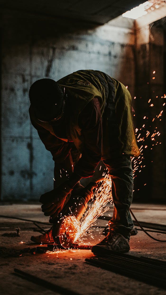 Worker in silhouette cutting metal with sparks in a construction site at sunset.